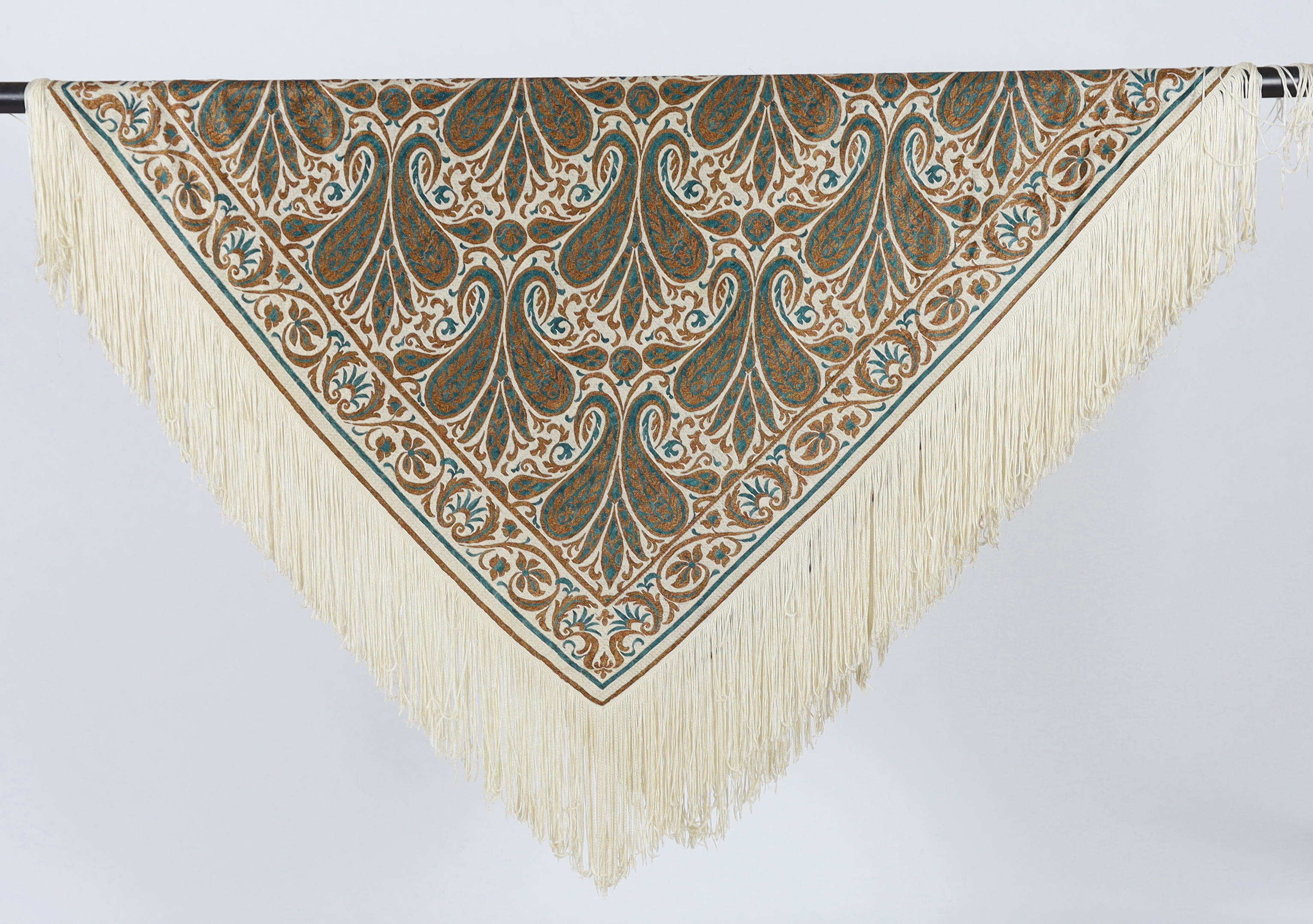 A 1920’s-1930’s cream silk woven shawl, woven with turquoise and bronze coloured silks in an all over tear drop paisley motif, edged with fine knitted cream fringing, approximately 109cm x 120cm